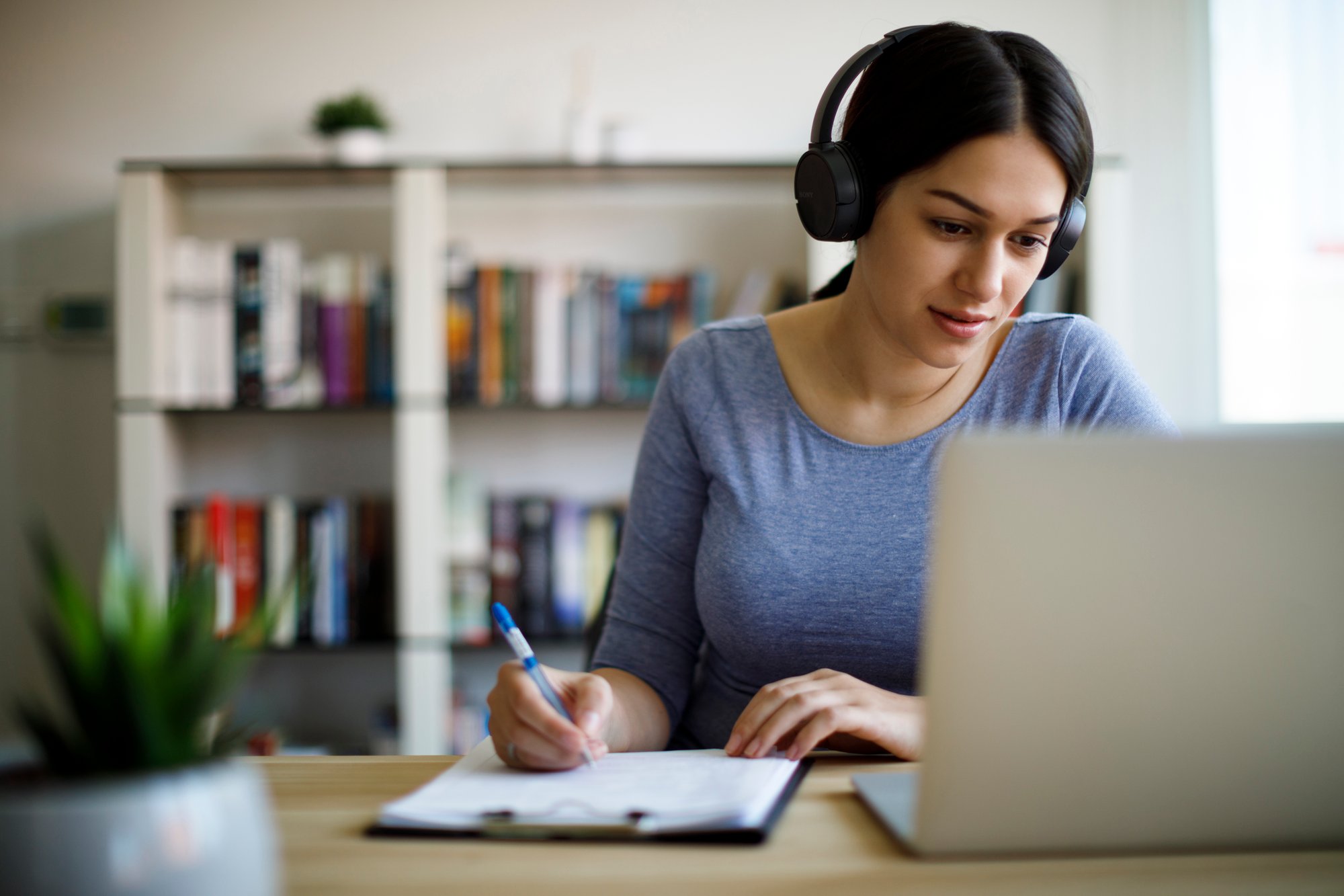 Young adult woman with headphones working at a laptop on a desk